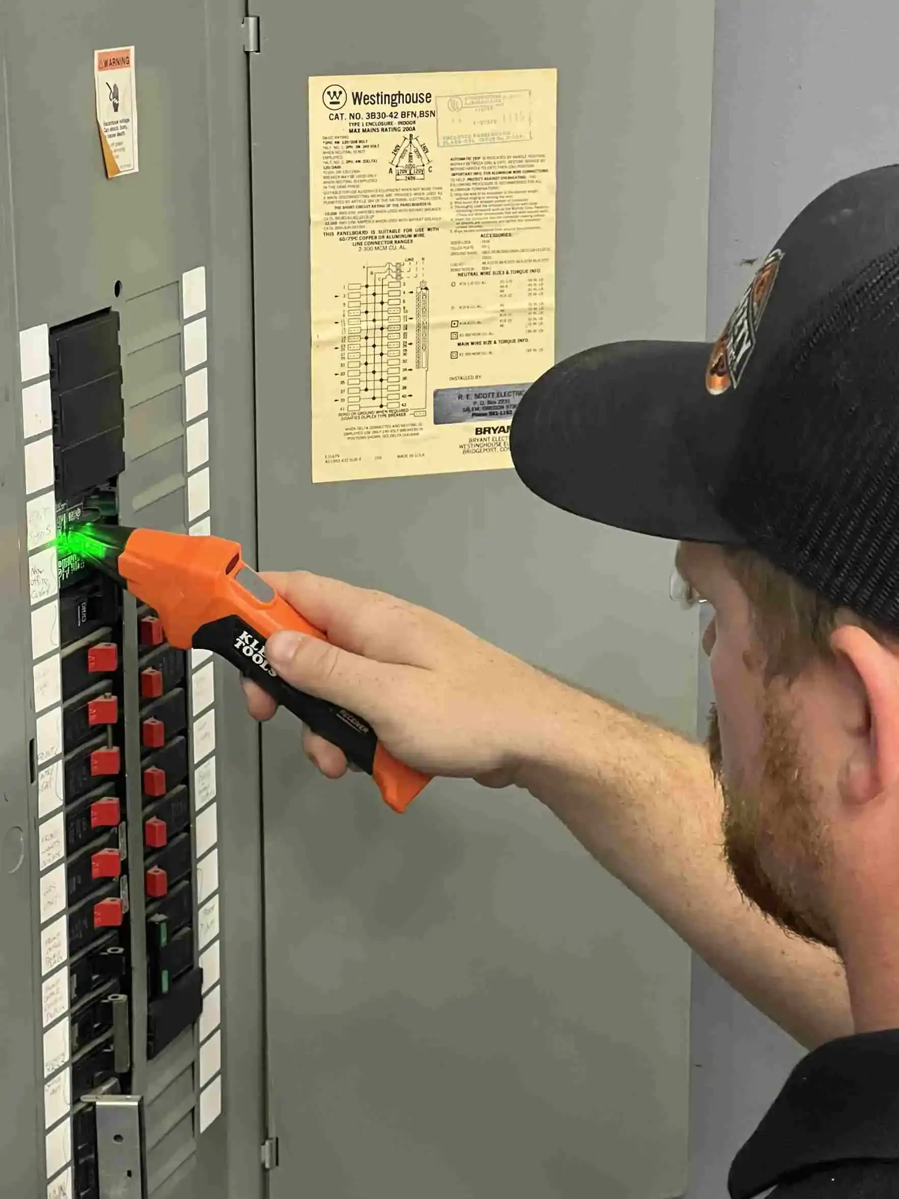 A man inspects an electrical panel with a laser tool, ensuring accurate measurements and safety compliance.